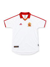Spain 2000 white adidas away jersey with a red fold-down collar, yellow V-neck accents, red shoulder stripes, red adidas logo, multicolored Spanish national team crest, and heritage hem label.