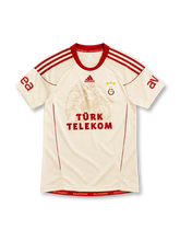 Galatasaray 2010/11 cream away jersey with tonal lion graphic, red adidas stripes and Türk Telekom sponsor