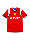 Manchester United 1984-86 home jersey, front view, red body, white sleeve panels with black and red trim, red white and black striped V-neck collar, Umbro diamond logo on sleeves, club crest, SHARP sponsor logo, striped ribbed cuffs