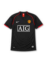 Manchester United 2007-08 away jersey, front view, black body with red piping, red and white striped collar tab, Nike swoosh logo, club crest, boxed AIG sponsor logo, red-trimmed cuffs