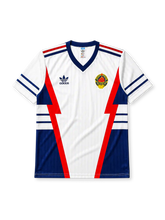 Yugoslavia 1990 World Cup away jersey, front view, white body with red and navy lightning bolt panels, navy V-neck collar, striped cuffs, adidas trefoil logo, national emblem