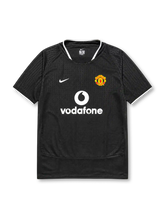 Manchester United 2003-04 away jersey, front view, black body with tonal geometric pattern, white ringer collar and cuffs, Nike swoosh logo, club crest, Vodafone sponsor logo