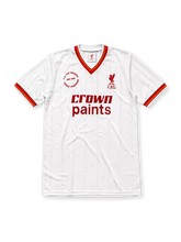 Liverpool 1985-86 away jersey, front view, white body with tonal pinstripe pattern, red V-neck collar with red and yellow stripe trim, striped cuffs, L.F.C. liver bird crest, red Crown Paints sponsor logo, circular 1985-1986 double winners badge on left chest
