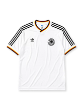 West Germany 1986 home jersey, front view, white body with black red and gold tricolor V-neck collar trim, black adidas trefoil logo and stripes, circular DFB eagle crest, tricolor trimmed cuffs