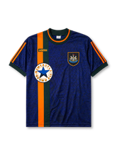 Newcastle United 1997-98 away jersey, front view, mottled navy body with orange and green vertical center stripe, dark green crew-neck collar with orange trim, green adidas logo, Newcastle United shield crest, circular Newcastle Brown Ale star sponsor badge