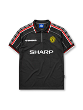 Manchester United 1998-99 third jersey, front view, black body, black white and red diamond pattern shoulder trim, black polo-style collar with zip placket, white Umbro logo, Manchester United devil crest, white Sharp sponsor logo