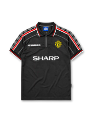 Manchester United 1998-99 third jersey, front view, black body, black white and red diamond pattern shoulder trim, black polo-style collar with zip placket, white Umbro logo, Manchester United devil crest, white Sharp sponsor logo