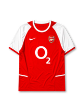 Arsenal 2002-04 home jersey, front view, red body with white raglan sleeves, white crew-neck collar with red trim, white Nike swoosh, Arsenal shield crest with cannon, large white O2 sponsor logo, white diagonal accent lines near hem