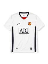 Manchester United 2008-09 away jersey, front view, white body with navy side panels, black V-neck collar with red inset and United text, black Nike swoosh, Manchester United crest, boxed AIG sponsor logo, NikeFIT wordmark near hem