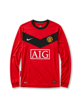 Manchester United 2010 home long-sleeve jersey, front view, red body with black chevron panel and long sleeves, black crew-neck collar, white Nike swoosh, Manchester United crest, boxed white AIG sponsor logo