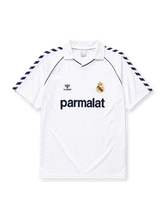 Real Madrid 1986-87 home jersey, front view, white body with navy Hummel chevron sleeve pattern, polo-style collar with navy piping, navy Hummel logo, Real Madrid crest with crown, navy Parmalat sponsor logo