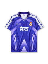 Real Madrid 1996-97 away jersey, front view, purple to blue gradient body with geometric triangle pattern, white sleeve panels with paw print pattern, purple polo-style collar, Kelme logo, Real Madrid crest with crown, white Teka sponsor logo
