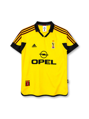 AC Milan 1999-2000 away jersey, front view, yellow body with black red striped shoulders, centenary emblem badge, adidas logo, Opel sponsor logo, 100 Milan collar text