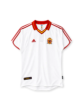 Spain 2000 away jersey, front view, white body, red fold-over collar with yellow stripe, red and yellow V-neck insert, red three stripes on shoulders and sleeves, red sleeve cuff trim, red adidas logo on right chest, Spanish coat of arms crest on left chest, black authentic licensed product badge at lower left hem, curved hem