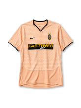 Juventus 2003-04 third jersey, front view, peach body with tonal houndstooth pattern, black-trimmed V-neck collar, Nike swoosh on right chest, oval Juventus crest with two gold stars on left chest, yellow FASTWEB sponsor logo on black band, black cuff trim, plain lower body panel