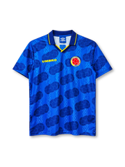 Colombia 1994 away jersey, front view, royal blue body with tonal diamond pattern and darker football-panel print, navy polo collar with yellow tipping and V insert, yellow UMBRO wordmark on right chest, Colombian Football Federation crest on left chest