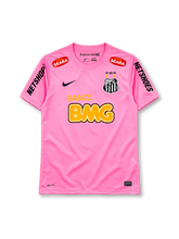 Santos 2013 pink jersey, front view, pink body, pink crew neck collar, red SEARA logos near shoulders, black NETSHOES lettering on sleeves, black Nike swoosh on right chest, Santos crest with two gold stars and 1912-2012 centenary crown on left chest, BANCO BMG sponsor logo, Nike Authentic tag at hem