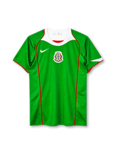 Mexico 2004 home jersey, front view, green body, white curved collar yoke with red trim, red piping down the front, white Nike swoosh on right chest, Mexican Football Federation crest centred on chest, red sleeve trim, white accent on left sleeve