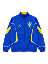 Front view of the Brazil 2026 Jordan anthem track jacket in royal blue with yellow curved sleeve and side panels, white piping, yellow Jumpman logo, five-star CBF crest, full zipper, and stand-up collar with yellow lining.