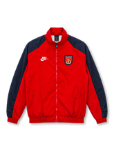 Front view of the Arsenal 1996/97 retro track jacket featuring a red body, navy shoulder and sleeve panels, white Nike logo, vintage Gunners shield crest, high stand-up collar, front zipper, two side pockets, and elasticated cuffs.
