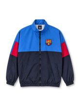 Front view of the FC Barcelona 1899 vintage track jacket featuring an electric blue upper body, navy lower panels, red sleeve accents, embroidered-style Barcelona crest, high stand-up collar, black front zipper, side pockets, and elasticated cuffs.