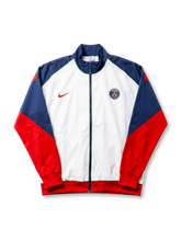 Paris Saint-Germain Nike track jacket with white body, navy raglan shoulder panels, red sleeves, red Nike Swoosh at left chest, and embroidered PSG crest at right chest