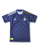Front view of Real Madrid special edition shirt in navy with gold monogram pattern, crest, trefoil-style chest logo, and striped shoulder detail.