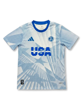 USA national team adidas 2026 FIFA World Cup pre-match jersey in white with allover blue halftone dot print, bold USA lettering at center chest, adidas logo at left, FIFA World Cup 2026 ball badge at right, royal blue crew collar, host nation badge at lower left hem