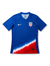 USA national team Nike 2024/25 away jersey in royal blue with tonal vertical pinstripe texture, dramatic diagonal red, white, and blue gradient fade at hem, white Swoosh at left chest, USA shield crest at right chest