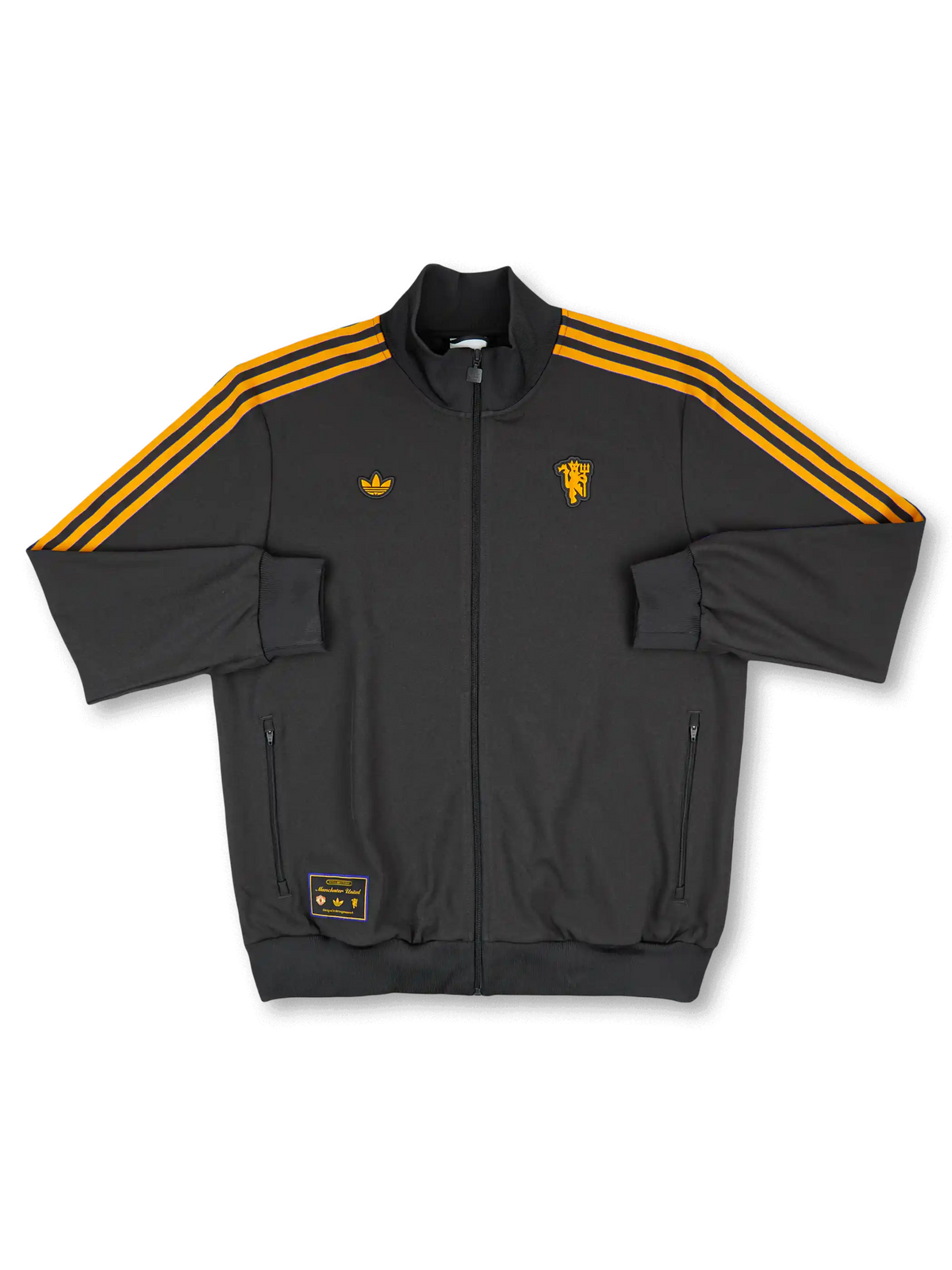 2025/26 Manchester United adidas Originals Icon short-sleeve track top in black with amber gold Three Stripes, gold standalone red devil crest at right chest, gold Trefoil at left chest, twin zip side pockets, and co-branded woven label at hem