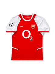 Front view of Arsenal 2002-04 home shirt with red body, white sleeves, O2 sponsor, Arsenal crest, and UEFA Champions League sleeve patch.