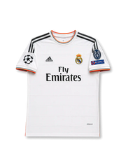 Front view of Real Madrid 2013-14 home shirt with white body, Fly Emirates sponsor, Real Madrid crest, grey shoulder stripes, orange trim, and UEFA Champions League sleeve patches.