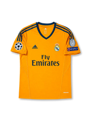 Front view of Real Madrid 2013-14 third shirt with orange base, Real Madrid crest, Fly Emirates sponsor, dark grey trim, and Champions League sleeve patch detailing.