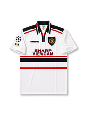 Front view of Manchester United 1997-99 away shirt with white base, black collar, red and black chest stripes, club crest, Sharp Viewcam sponsor, and Champions League sleeve patch.