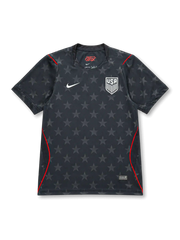 USA 2026/27 away shirt with a dark charcoal base, tonal all-over star pattern, white USA shield crest, white chest Swoosh, red piping accents, and V-neck collar.