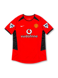 Manchester United 2002-04 home jersey by Nike, featuring a classic red soccer shirt with a black crew neck collar, black sleeve trim, angular black shoulder and side panels, white Nike Swoosh, Vodafone sponsor logo, and Manchester United club crest, representing the 2002-03 and 2003-04 seasons.