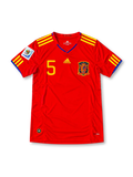 Front view of the Spain 2010 red home football jersey featuring Carles Puyol number 5, yellow Adidas shoulder stripes, blue neckline detailing and the Spanish national team crest.