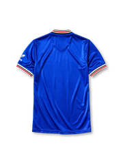 Manchester United 1985-86 third jersey, front view, royal blue body, white striped V-neck collar, white sleeve panels with black and red trim, adidas trefoil logo on sleeve, club crest, SHARP sponsor logo, striped ribbed cuffs