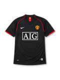 Manchester United 2007-08 away jersey, front view, black body with red piping, red and white striped collar tab, Nike swoosh logo, club crest, boxed AIG sponsor logo, red-trimmed cuffs