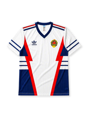 Yugoslavia 1990 World Cup away jersey, front view, white body with red and navy lightning bolt panels, navy V-neck collar, striped cuffs, adidas trefoil logo, national emblem