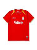Liverpool 2005-06 home jersey, front view, red body with gold shoulder panels and collar trim, V-neck collar, white Reebok logo, Liverpool crest with five stars, Carlsberg sponsor logo, small winner's patch near bottom hem