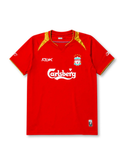 Liverpool 2005-06 home jersey, front view, red body with gold shoulder panels and collar trim, V-neck collar, white Reebok logo, Liverpool crest with five stars, Carlsberg sponsor logo, small winner's patch near bottom hem