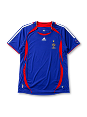 France 2006 home jersey, front view, royal blue body with red crew-neck collar and piping, curved red side panels, white adidas logo and stripes, gold F.F.F. rooster crest with star, small 2006 World Cup emblem near hem, ClimaCool tag