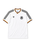West Germany 1986 home jersey, front view, white body with black red and gold tricolor V-neck collar trim, black adidas trefoil logo and stripes, circular DFB eagle crest, tricolor trimmed cuffs