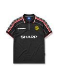 Manchester United 1998-99 third jersey, front view, black body, black white and red diamond pattern shoulder trim, black polo-style collar with zip placket, white Umbro logo, Manchester United devil crest, white Sharp sponsor logo