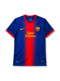 Barcelona 2012-13 home jersey, front view, blue body with red gradient center panel, red crew-neck collar, yellow Nike swoosh, Barcelona crest, yellow Qatar Foundation sponsor logo, red cuffs