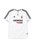 Real Madrid 2003-04 home jersey, front view, white body, black V-neck collar with button placket, black adidas logo and stripes, Real Madrid crest with crown, black and red Siemens mobile sponsor logo