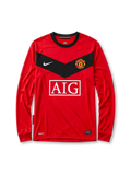 Manchester United 2010 home long-sleeve jersey, front view, red body with black chevron panel and long sleeves, black crew-neck collar, white Nike swoosh, Manchester United crest, boxed white AIG sponsor logo