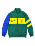 Front view of a Brazil national team retro track jacket featuring a deep green body, bright yellow chest band, royal blue left sleeve, yellow-striped right sleeve, green Nike Swoosh, five-star CBF crest, full zipper, and stand-up collar.