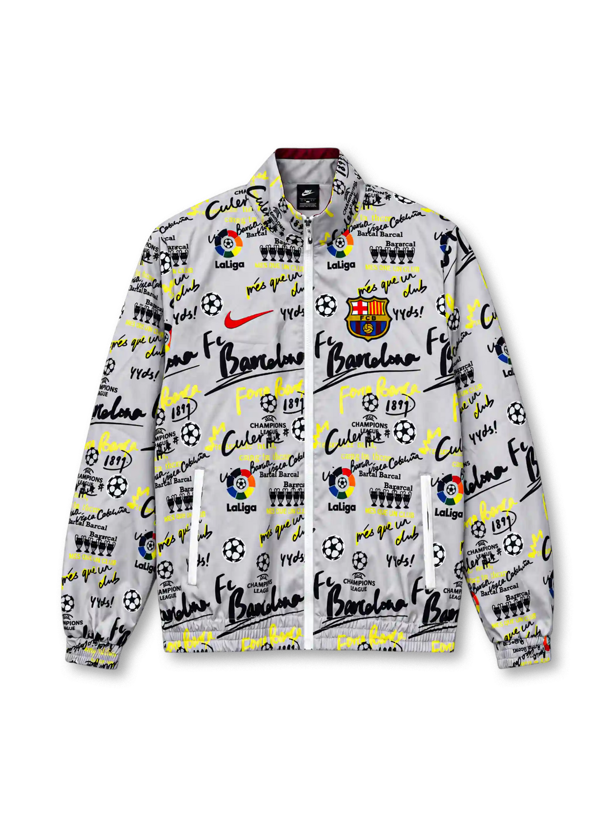 Front view of a white FC Barcelona-inspired graffiti track jacket featuring black and neon yellow lettering, soccer ball and trophy graphics, LaLiga-inspired motifs, a red Nike Swoosh, colorful Barcelona crest, full zipper, and elasticated cuffs.